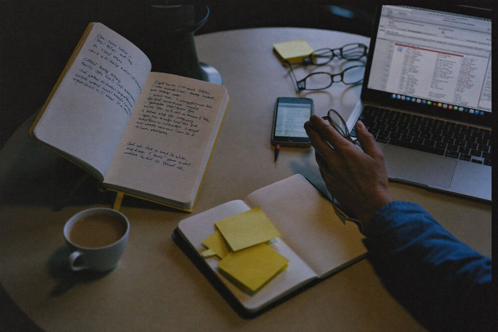 Le soir à la table de la cuisine : carnet de commandes manuscrit, téléphone avec les messages et tableur ouvert sur l'ordinateur