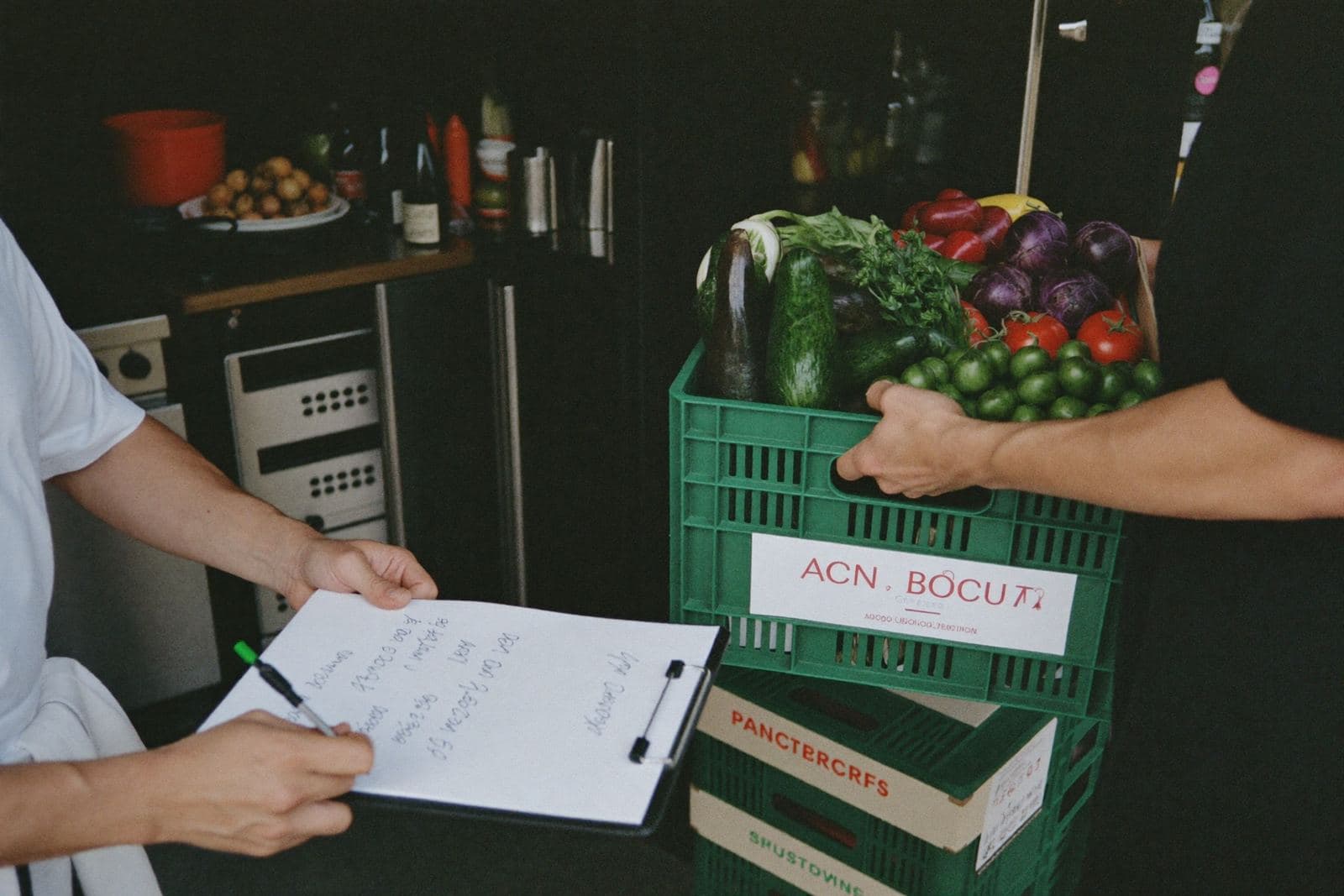 Livraison du matin à la porte de la cuisine : la caisse de légumes change de mains, le bon de livraison se signe sur place